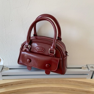 Close-up of a burgundy mini Boston bag featuring shiny PU leather and a front flap pocket