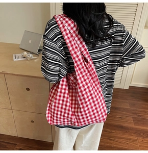 Lifestyle shot of red and white gingham canvas tote bag worn by a model in a cozy room