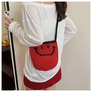 Detail of red crochet bucket bag featuring a black knit smiley face and long shoulder strap