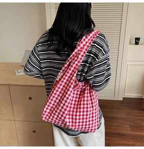 Detail view of red checkered canvas tote bag showing soft drape and wide shoulder strap