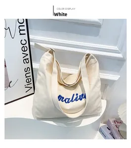 Detail shot of white canvas tote bag with blue 'maliu' embroidery on a display stand