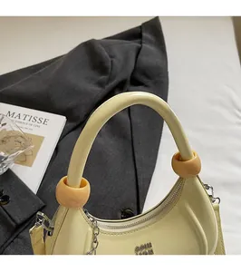 Close-up of cream crescent handbag with patent leather finish and round bead detail