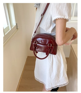 Detail of burgundy glossy leather handbag with oval logo and silver hardware