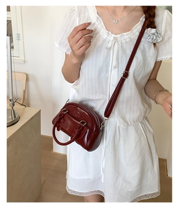 Close-up of wine red leather Boston bag with embossed logo on a white dress model
