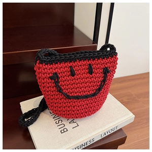 Close-up of red knit bucket bag featuring a black woven smiley face and thick cotton cord texture