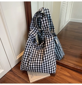 Detail of black and white gingham canvas tote bag on dark wooden floor with mirror reflection