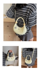 Detail view of cream crescent bag with wooden bead handle and metal G pendant charm