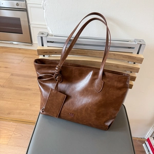 Close-up of dark brown leather tote bag showing grainy texture and small accessory pouch