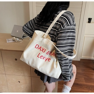 Rückansicht eines Models mit großer cremefarbener Canvas-Tasche und rotem Buchstaben-Stick