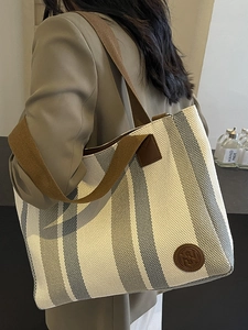 Striped canvas tote bag with wide brown shoulder strap worn by a model in a beige suit