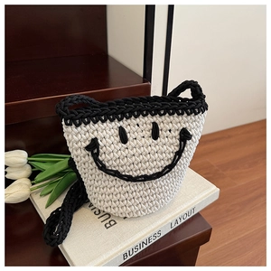 Detail of a knit smiley face bucket bag in cream cotton with black contrast handles