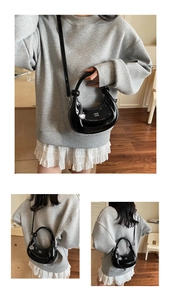 Detail of black patent leather crescent bag with white lettering and metal G pendant