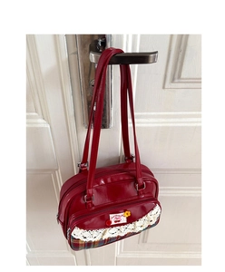 Détail du sac à carreaux rouges avec écusson cerise, bordure dentelle et aspect brillant
