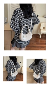 Detail of creamy moon bag with glossy finish and stylish metallic G-pendant decoration
