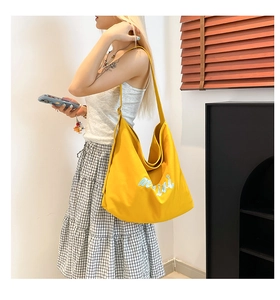 Detail of yellow canvas tote bag with blue mimi embroidery and casual shoulder strap