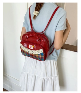 Détail du sac à dos en cuir verni rouge avec bordure en dentelle et badge cerise