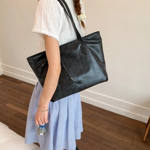 Detailed macro view of black leather tote bag with front zipper pocket and embossed logo