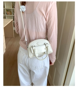 Detail view of a cream leather Boston bag with metal logo and slender crossbody strap