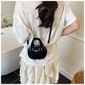 Mini black velvet bowling bag featuring a silver bow detail worn by a model in a dress