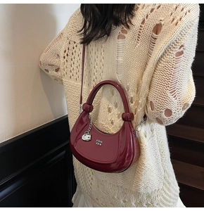 Detail of burgundy patent leather crescent bag featuring a metallic G logo and sleek handle