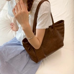 Detail of vintage brown PU leather tote bag featuring brand logo and small hanging pouch