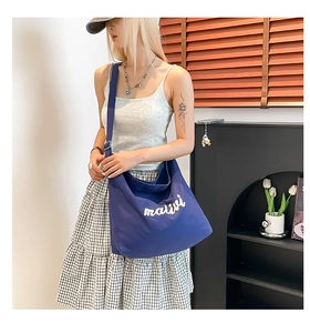 Detail view of the deep blue canvas tote bag with white mailvi embroidery on a model