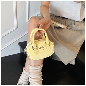 Detail of light yellow mini Boston bag with metal bow accent and silver zipper texture