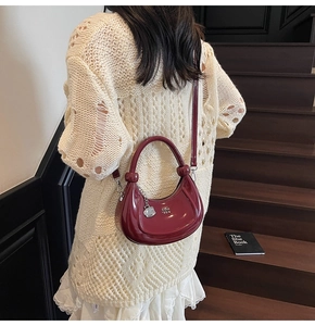 Detail of burgundy glossy patent leather hobo bag with silver logo and knot handle