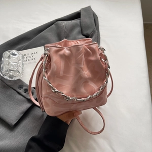 Sac seau rose avec chaîne argentée et texture de lettres abstraites sous une lumière douce