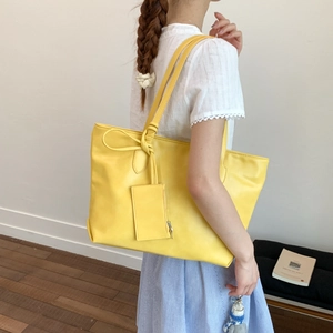 Detail of a bright yellow leather tote bag with a matching small hanging card pouch accessory