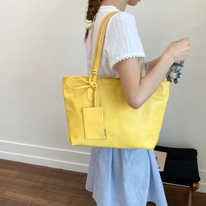 Detail of yellow leather tote bag featuring white PAN TOR logo and small hanging pouch