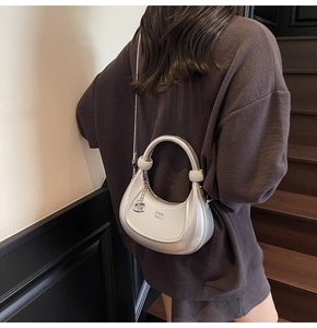 Rear view of model holding silver hobo bag with metal chain strap and G charm detail