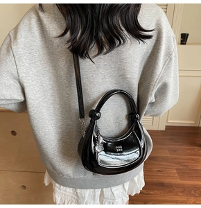 Model wearing a glossy black patent leather crescent bag with a metallic ring handle