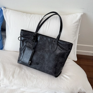 Detail of black leather tote bag featuring embossed logo and matching mini pouch accessory