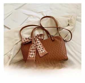 Close-up of brown textured tote bag with wave pleated design and checkered bow scarf