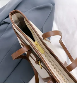 Detailed top view of the beige tote bag showing its gold zipper and textured lining
