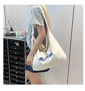 Detail of white canvas tote bag with blue embroidered letters and wide shoulder strap
