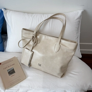 Detail of beige leather tote bag with metal logo and small hanging zipper pouch