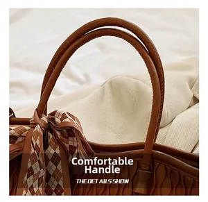 Detail of brown tote bag featuring wavy texture and handle with a checkered scarf tie