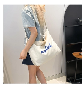 Detail of canvas tote bag featuring blue artistic embroidery and wide shoulder strap