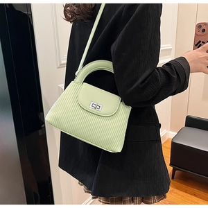 Detail view of light green striped crossbody bag with silver metal lock on black outfit