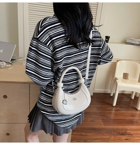 Detail of a chic cream-colored hobo bag with gold metal logo and crossbody strap
