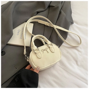 Detail view of mini cream bowling bag with silver bow on grey suit and white fabric