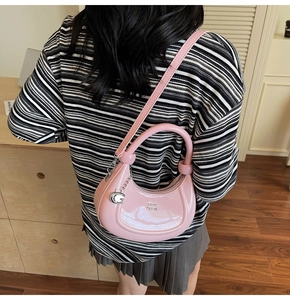 Pink glossy patent leather half moon bag with metal logo detail worn by a model