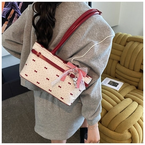 Détail d'un sac bandoulière blanc avec motifs nœuds rouges et pendentif cœur