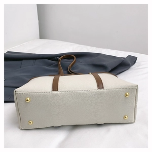 Detail view of beige leather tote bag base with protective gold metal studs and brown strap