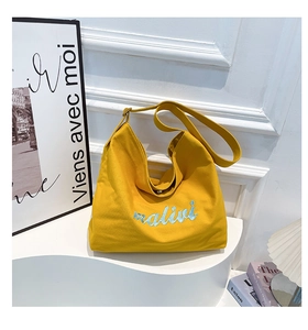 Detailed close-up of yellow canvas tote bag featuring blue malivi embroidery and wide strap