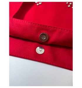 Detailed macro view of the silver magnetic buckle on a red canvas tote with metal studs