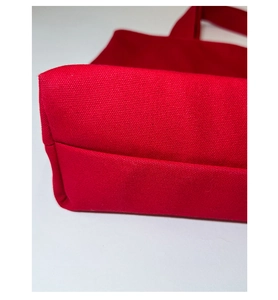 Close-up detail of reinforced bottom stitching on red canvas tote bag with star rivets
