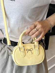 Mini pale yellow bowling handbag with golden bow detail and slim crossbody strap